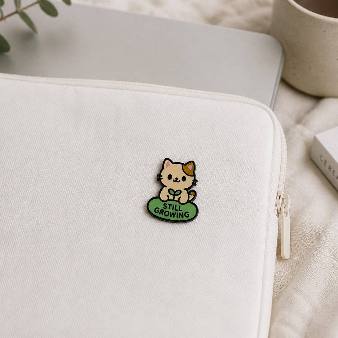 Still Growing Cat enamel pin featuring a cute cartoon cat with a plant sprout on its head, pink and green colors, on a white background.