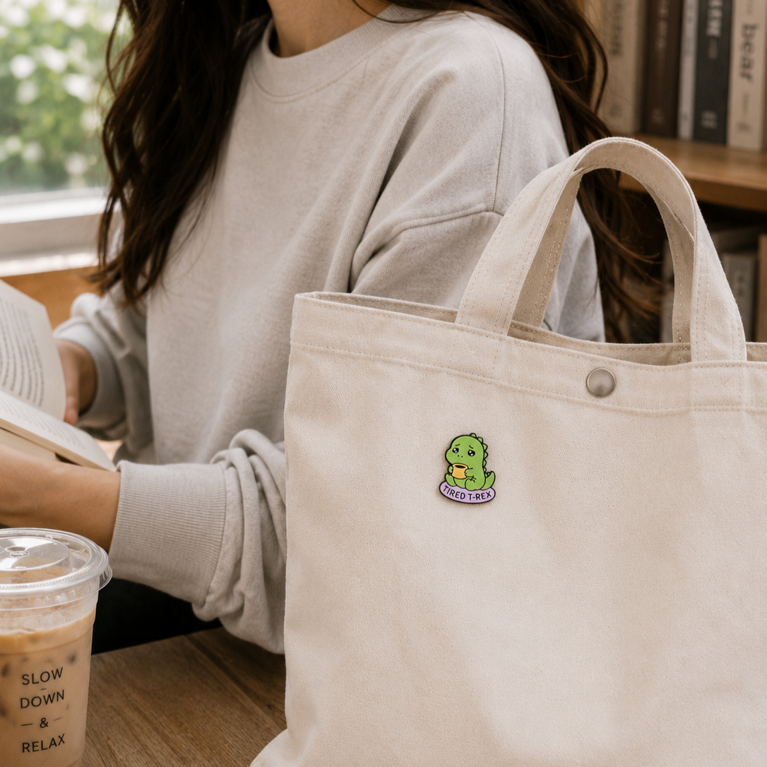 Tired T-Rex enamel pin featuring a sleepy dinosaur with droopy eyes and a relaxed posture, pinned on a white background.