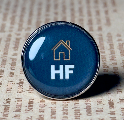 Close-up of a Pinlord.com lapel pin featuring the "Now Review" design on a plain background.